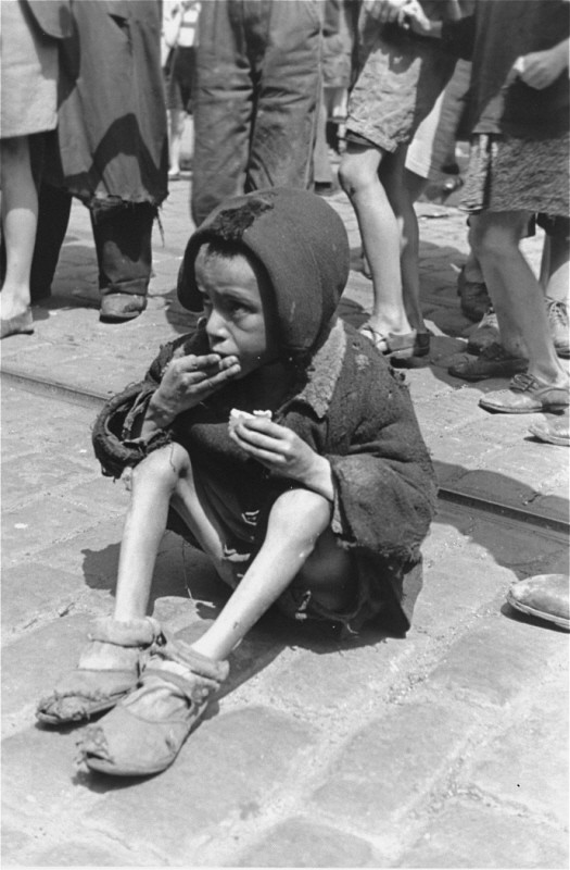 An emaciated child eats in the streets of the Warsaw ghetto. [LCID: 89469]